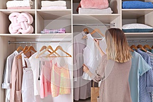 Woman choosing outfit from large wardrobe closet with stylish clothes