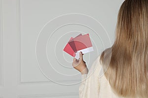 Woman choosing paint shade for wall indoors, focus on hand with color sample cards. Interior design