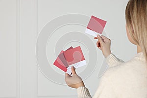 Woman choosing paint shade for wall indoors, focus on hands with color sample cards. Interior design