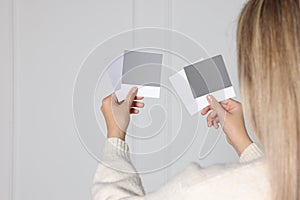 Woman choosing paint shade for wall indoors, focus on hands with color sample cards. Interior design