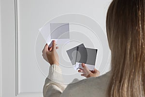 Woman choosing paint shade for wall indoors, focus on hands with color sample cards. Interior design