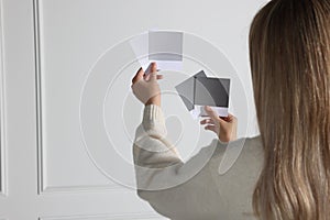 Woman choosing paint shade for wall indoors, focus on hands with color sample cards. Interior design