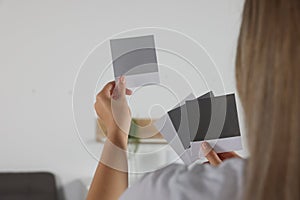 Woman choosing paint shade for wall in room, focus on hands with color sample cards. Interior design