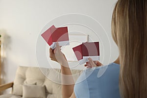 Woman choosing paint shade for wall in room, focus on hands with color sample cards. Interior design