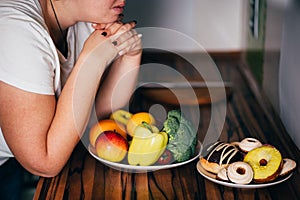 Woman choosing between sweets and healthy food