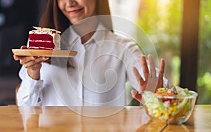 A woman choosing to eat cake and making hand sign to refuse vegetables salad