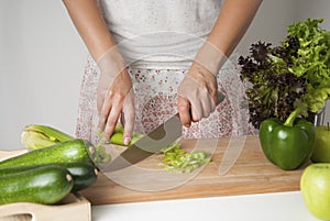 Woman chopping celery vegetable, preparing food in her kitchen, she is cutting fresh celery on a cutting board with a knife.