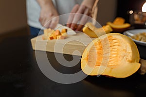 Woman chopping pumpkin on kitchen board, only hands visible. Autumn seasonal vegetables cooking.