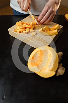 Woman chopping pumpkin on kitchen board, only hands visible. Autumn seasonal vegetables cooking. Healthy eating habits
