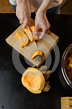 Woman chopping pumpkin on kitchen board, only hands visible. Autumn seasonal vegetables cooking. Healthy eating habits