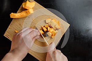 Woman chopping pumpkin on kitchen board, only hands visible. Autumn seasonal vegetables cooking. Healthy eating habits