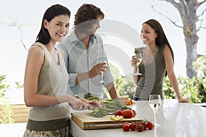 Woman Chopping Vegetables With Friends Communicating At Kitchen Counter