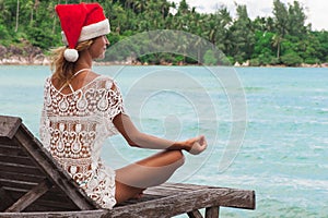 Woman in christmas hat meditating in a yoga pose at thel beach photo