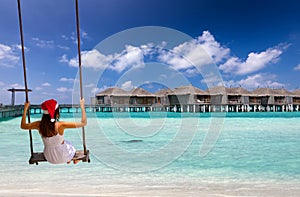 Woman with Christmas hat on a swing in front of a tropical beach