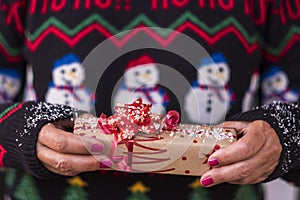 Woman in Christmas sweater holding and offering a surprise gift in a recycled paper with a dusting of white snow