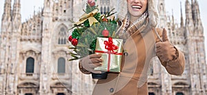 Woman with Christmas tree and gift in Milan showing thumbs up