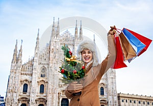 Woman with Christmas tree and shopping bags in Milan rejoicing