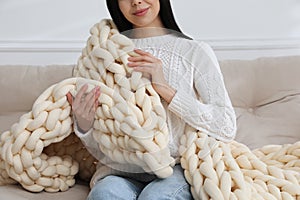 Woman with chunky knit blanket on sofa at home, closeup