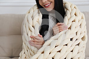 Woman with chunky knit blanket on sofa at home, closeup