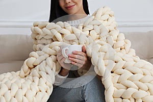 Woman with chunky knit blanket on sofa at home, closeup