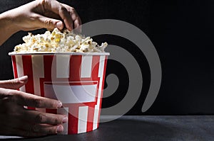 Woman in the cinema eating popcorn.A large bucket of salty popcorn against black wall.Empty space fo text