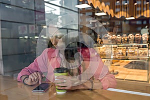 woman in a city cafe in summer reads social networks in Internet application. Background of coffee tea pastries showcase