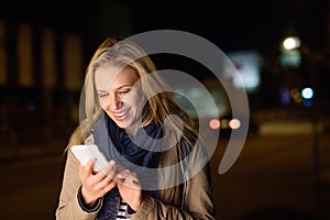 Woman in the city at night holding smartphone, texting.