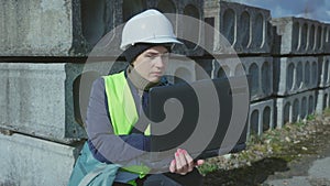 Woman civil engineer writing data on laptop near concrete panels