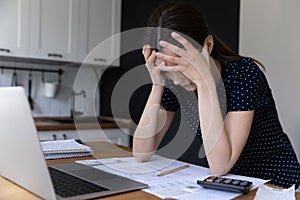 Woman clasping head lean at table with heap of bills