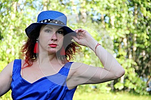 Woman in a classic blue short dress and blue classic hat. red hair and earrings