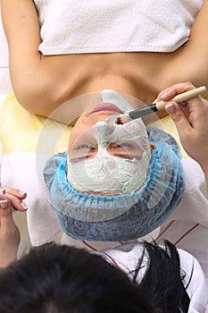 Woman with clay facial mask in beauty spa.