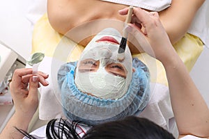 Woman with clay facial mask in beauty spa.