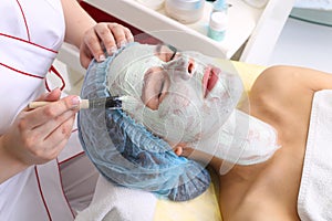 Woman with clay facial mask in beauty spa.