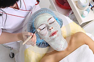 Woman with clay facial mask in beauty spa.