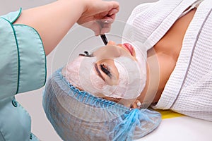 Woman with clay facial mask in beauty spa.