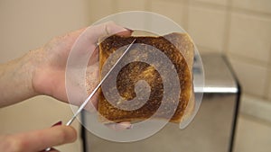 Woman clean the ashes with a burnt toast with a knife. Toasted bread in a toaster