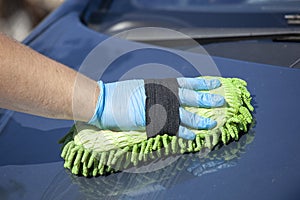 Woman clean blue car in glowes, green sponge in hand