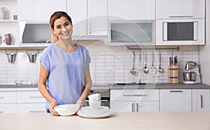 Woman with clean dishes near table in kitchen