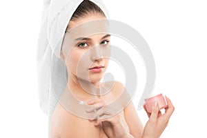Woman with clean face and towel on her head applying moisturizer cream at shoulders. Isolated.