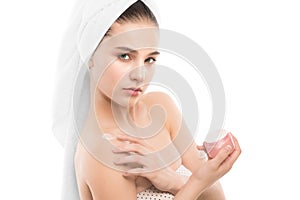 Woman with clean face and towel on her head applying moisturizer cream at shoulders. Isolated.