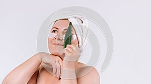 A woman with clean skin and a towel on her head holding a aloe vera leaf in her hands. Healthy skin care concept on