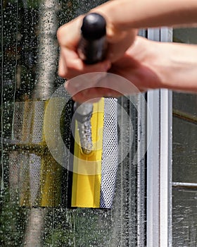 woman cleaner wiping window glass with a telescopic MOP outside a suburban private home, close-up, window washing concept with wat