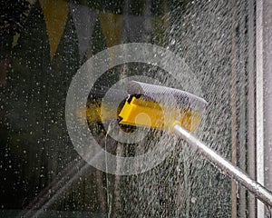woman cleaner wiping window glass with a telescopic MOP outside a suburban private home, close-up, window washing concept with wat