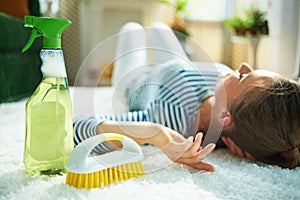 Woman with cleaning agent and brush laying on carpet