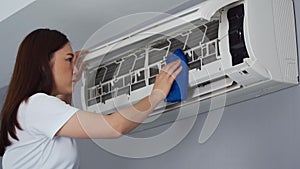 Woman cleaning the air conditioner with cloth at home