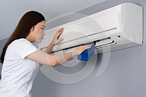 Woman cleaning the air conditioner with cloth at home