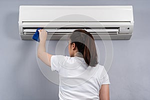 Woman cleaning the air conditioner with cloth at home