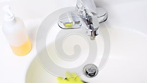 Woman is cleaning bathroom sink with detergent in yellow rubber gloves