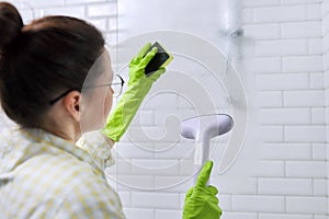 Woman cleaning in bathroom, washing glass with shower steam