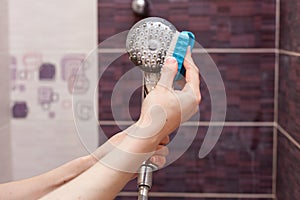 Woman cleaning an calcified shower head in domestic bathroom with small brush